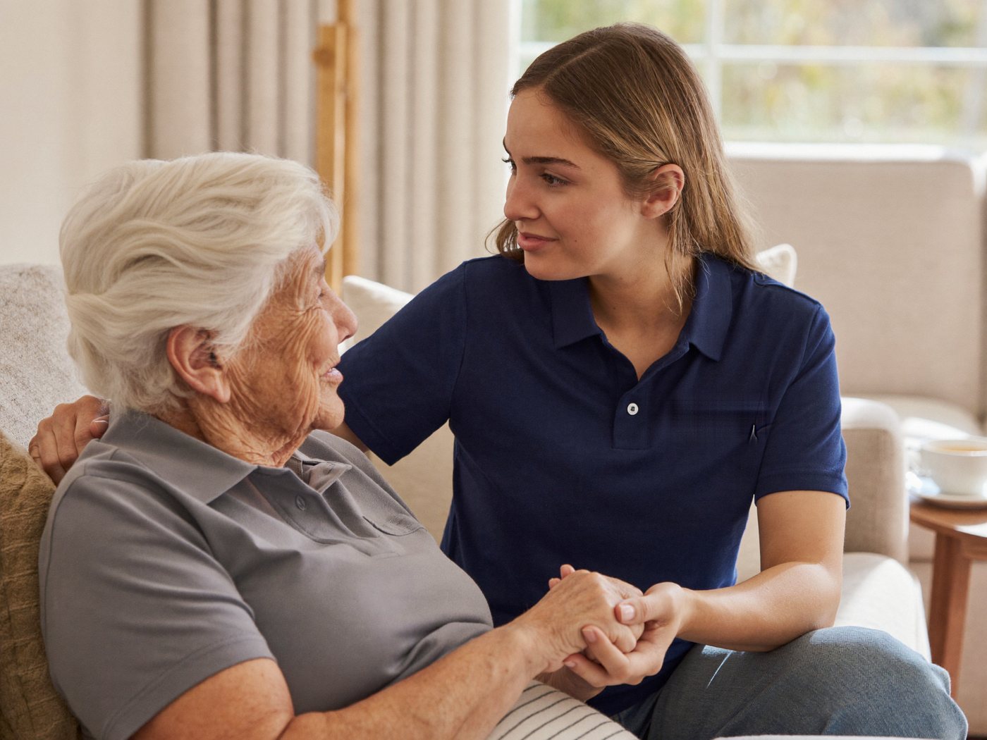 A support worker sitting with an older woman in her living room, holding her hand as they talk